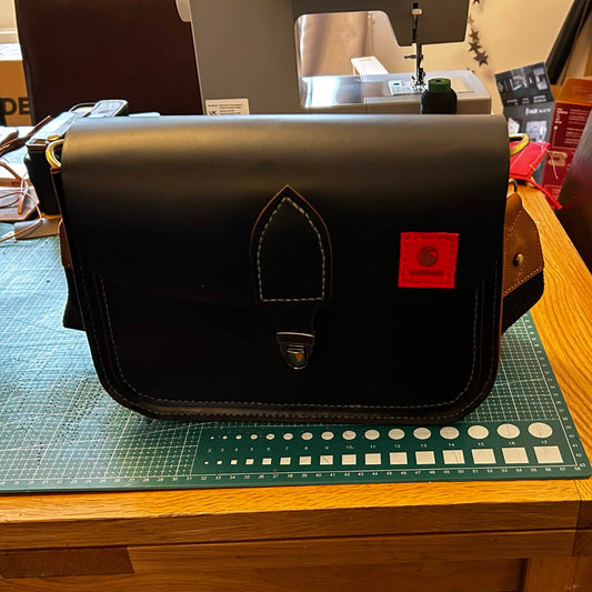 Custom black leather shoulder bag with white stitching and a red label on the workshop table