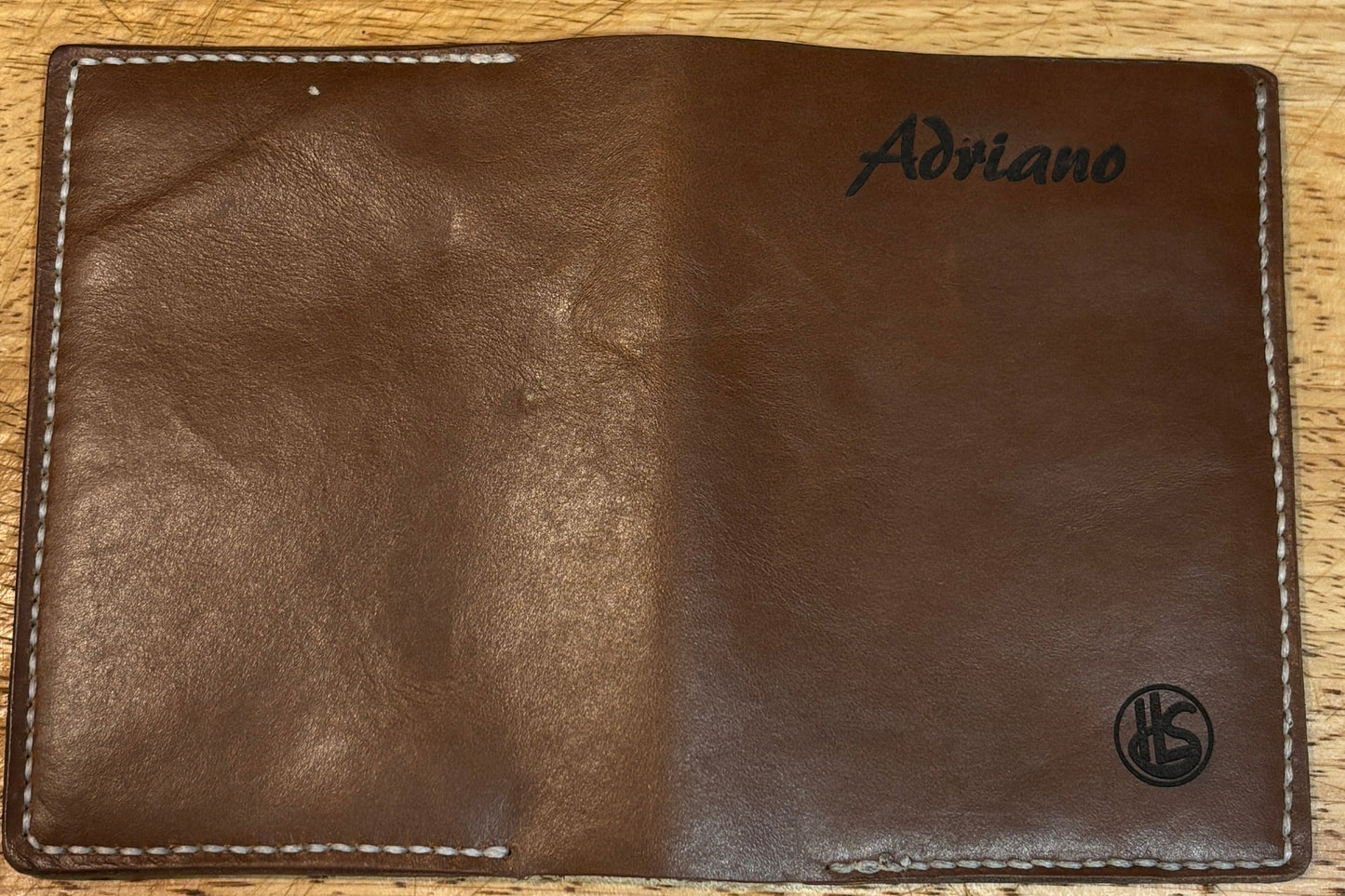 Brown leather wallet with branding on a wooden surface.