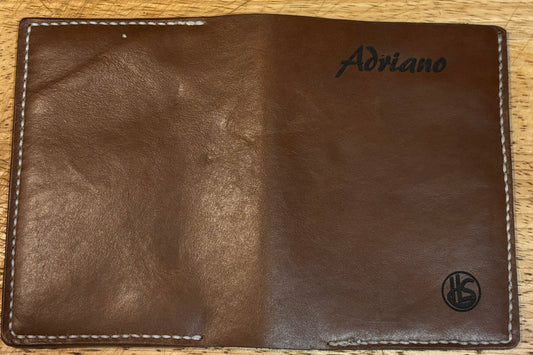 Brown leather wallet with branding on a wooden surface.